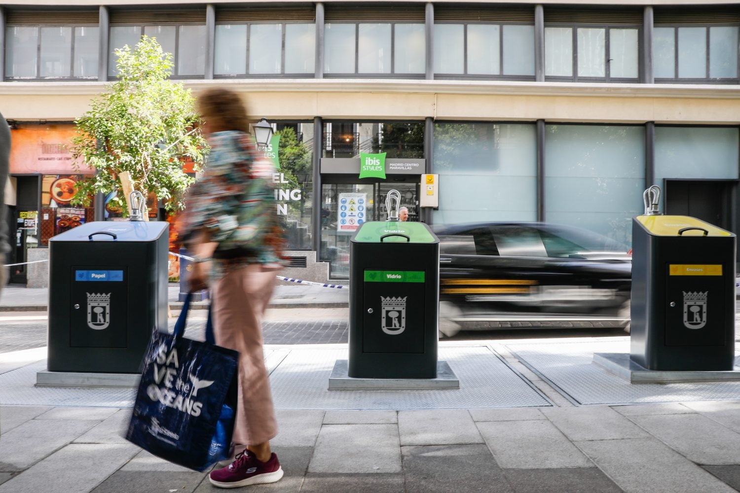 Viandante pasa por delante de contenedores de basura en Madrid-Imagen de archivo